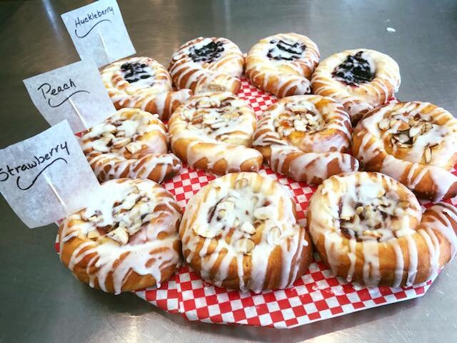 Assorted fruit danishes on a red and white checkered tray, featuring flavors like huckleberry, peach, and strawberry, topped with icing and almonds.