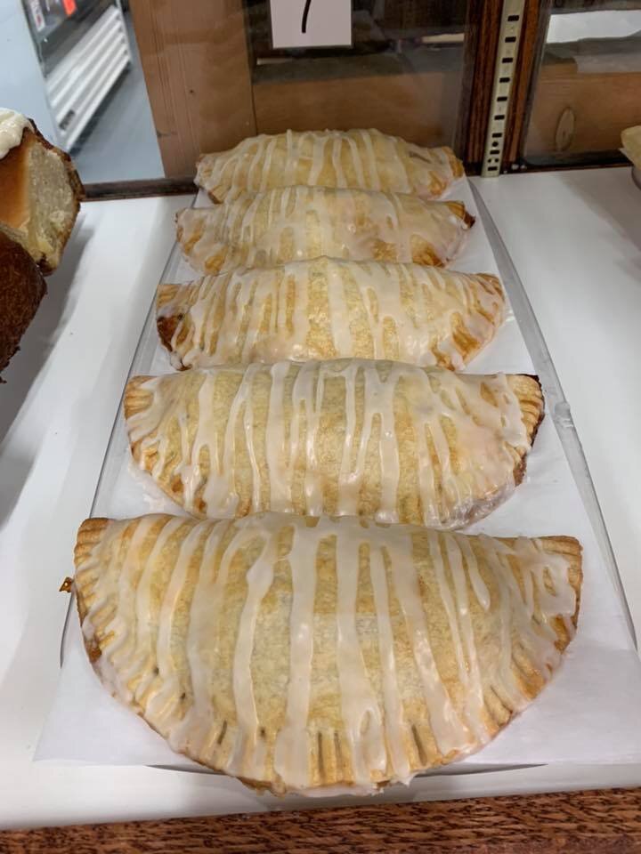Freshly baked pastries drizzled with icing, displayed in a bakery case. The golden-brown, flaky crusts are filled with sweet filling, showcasing a tempting dessert option for customers.