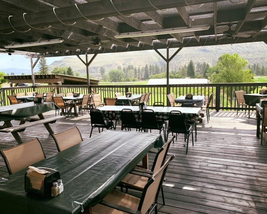 Outdoor dining area with multiple tables and chairs, featuring a scenic view of mountains and greenery, ideal for enjoying meals in a relaxed atmosphere.