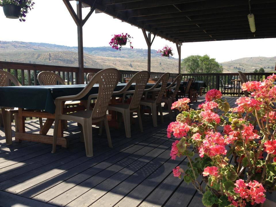 Outdoor dining area with plastic chairs and tables, surrounded by vibrant pink flowers and scenic mountain views in the background. Perfect for enjoying meals in a natural setting.
